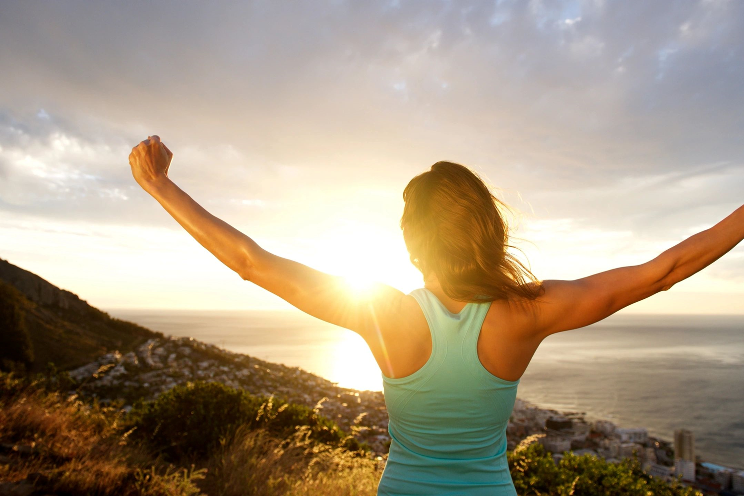 A woman standing on top of a hill with her arms in the air.