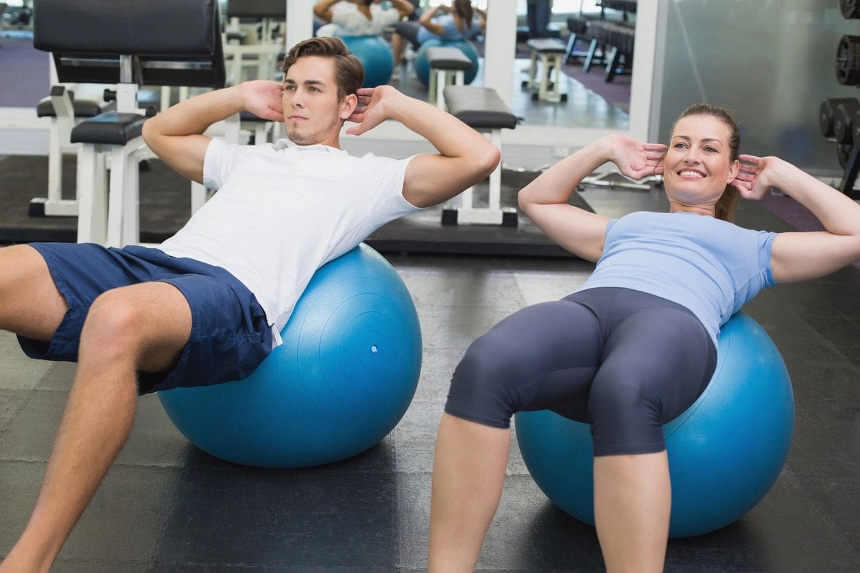 Two people are doing sit ups on exercise balls.