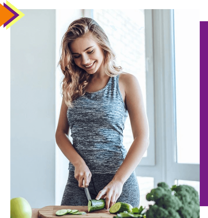 A woman cutting broccoli in front of some vegetables.