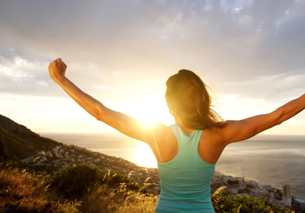 A woman standing on top of a hill with her arms in the air.